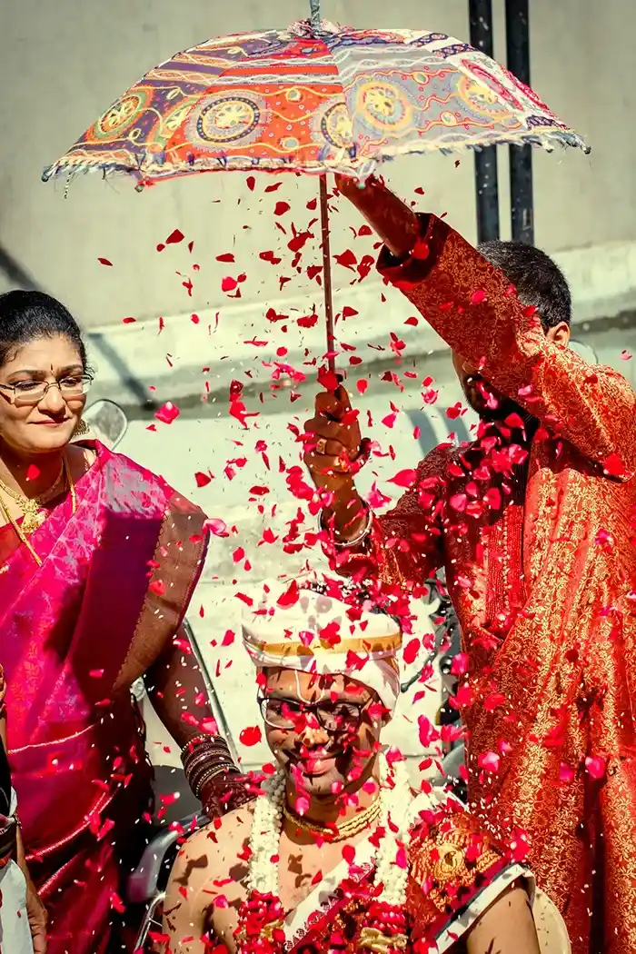 A vibrant Indian wedding scene with rose petals showered over a seated groom.